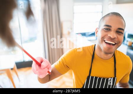 Portrait of young latin man cleaning his new house with a duster. Housekeeping and cleaning concept. Stock Photo