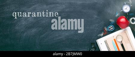 School stationary on chalkboard. Notebooks, pen, pencil, alarm clock, red apple and other tools. Banner with inscription Quarantine. Stock Photo