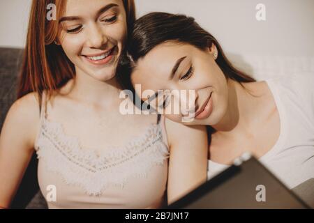 Two caucasian sisters are having joy together while smiling and using a tablet on the sofa Stock Photo