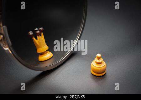 Pawn looking in the mirror and seeing himself like a king with dark background. Psychological concept Stock Photo