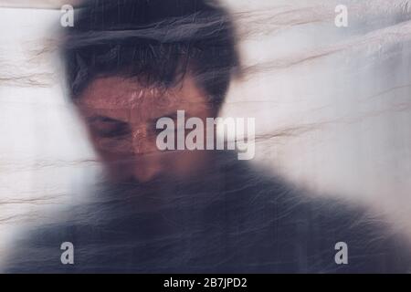 Mental health disorder, depressed man behind plastic curtain. Portrait of sad adult male, selective focus. Stock Photo