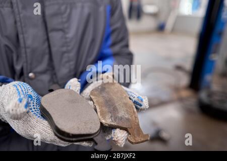 The mechanic holds the old and new brake pads in his hand. Change the old to new brake disc on car in a garage. Auto repair concept. Stock Photo