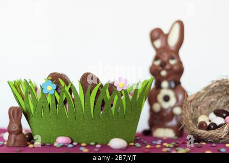 Easter basket with chocolate eggs, chocolate bunny, nest with almonds and sweets on table against white background Stock Photo