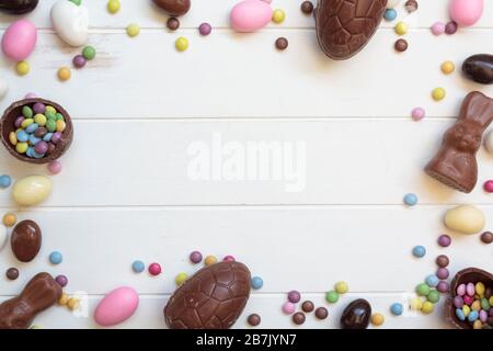 Top view of chocolate eggs, chocolate bunny, easter almonds and sweets on white wooden table with copy space. Easter frame composition Stock Photo