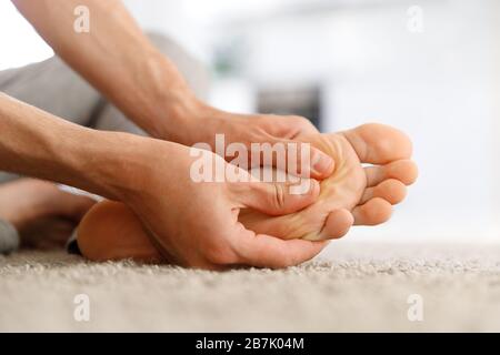 Man hands giving foot massage to yourself to relieve pain after a long walk, suffering with flat feet, close up, soft focus, indoors. Flat feet, leg f Stock Photo