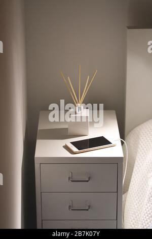 Aromatic reed air freshener and smartphone on charge on the bedside table at night at home. Stock Photo