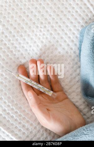 Sick man holding a oral mercury thermometer in his hand, showing high temperature, lying in bed, copy space. Cold, illness, flu season concept Stock Photo
