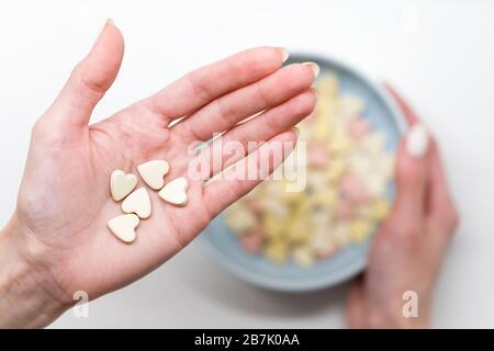 Close up of woman hold heart shaped vitamins or mineral pills on palm, blurred hand holding bowl of colorful vitamins on white background, top view. F Stock Photo