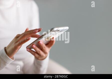 Close up of female hands typing text message, using modern smartphone device in marble case, sitting in white chair, touches the touchscreen with a fi Stock Photo