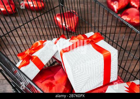 black metal basket full of white gift boxes with a red satin ribbon and a red large bow. Lifestyle Image for sale, gifts, shopping and giveaway Stock Photo