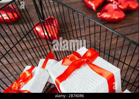 black metal basket full of white gift boxes with a red satin ribbon and a red large bow. Lifestyle Image for sale, gifts, shopping and giveaway Stock Photo