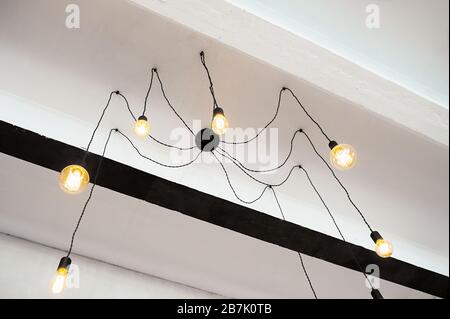 Unusual black loft chandelier on a white ceiling. The chandelier looks like a spider. Stock Photo