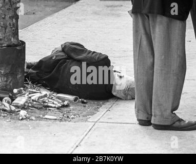 July, 1970, film image of drunk alcoholic laying in the street of New York City with another man standing near him in everyday life. Stock Photo