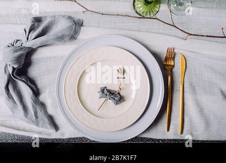 Eco-friendly natural table setting. Two white vintage plates with a gold fork and a gold knife and a cotton blue-gray napkin on a white vintage tablec Stock Photo