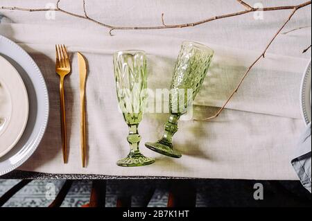 Two empty green vintage shaped drink glasses on a cotton old tablecloth, top view, hard light. Table setting in a mysterious spring style with live pl Stock Photo