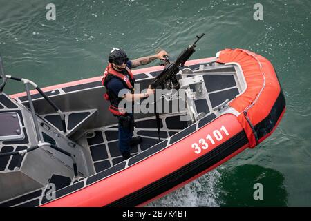 Coast Guard member stands ready with gun on US Coast Guard boat as he patrols the Atlantic Ocean coastline Stock Photo