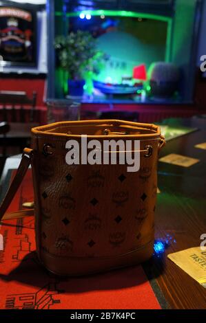 MCM Leather handbag at the bar in a UK pub with green lit window in background Stock Photo