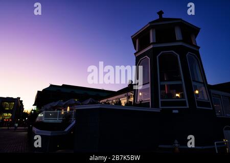 ALEXANDRIA, Virginia, United States — The Old Town Alexandria waterfront at dusk, with the distinctive tower of the Chart House restaurant visible in the foreground. The historic waterfront, located along the Potomac River, offers a blend of colonial architecture and modern amenities. Alexandria's riverside setting provides picturesque views of the illuminated cityscape as day transitions to night. Stock Photo