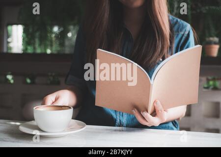 Closeup image of an asian woman reading a book while drinking coffee in modern cafe Stock Photo