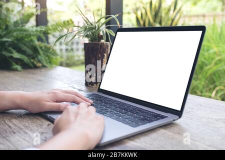 Mockup image of a woman using and typing on laptop with blank white desktop screen on wooden table and green nature background Stock Photo