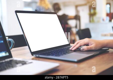 Mockup image of woman's hands using and typing on laptop with blank white desktop screen on wooden table in office Stock Photo