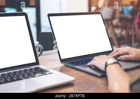 Mockup image of woman's hands using and typing on laptop with blank white desktop screen on wooden table in office Stock Photo