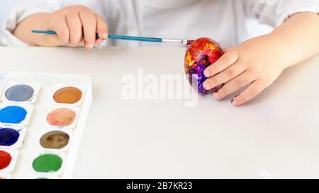 Child hands painted Easter eggs, time at home, paints and brushes on white table. Preparation for the Easter. Idea how to keep children at home on time for coronavirus and quarantine. Stock Photo