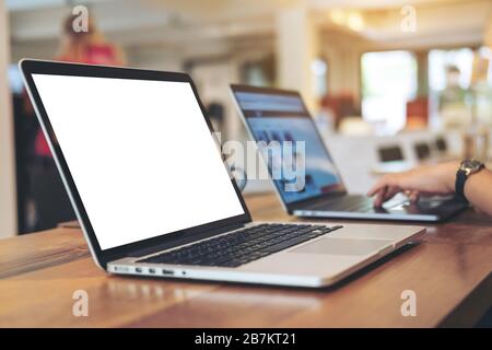 Mockup image of woman's hands using and typing on laptop with blank white desktop screen on wooden table in office Stock Photo