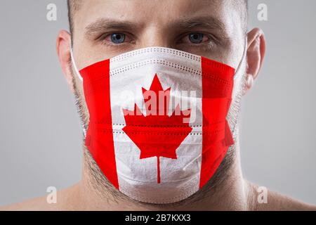 Young man with sore eyes in a medical mask painted in the colors of the national flag of Canada. Medical protection against airborne diseases, coronav Stock Photo