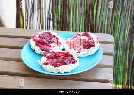 Closeup shot of three rice crackers with raspberry jam on a blue plate on a wooden table Stock Photo