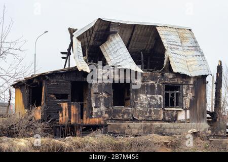 A sinful house, arson incident. Broken roof and glass windows, charred walls. Black rural cottage after a fire. Arson of a one-story private house, pr Stock Photo