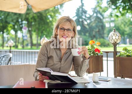 Portrait of successful beautiful middle-aged blonde woman in summer outdoor restaurant. Businesswoman having coffee break Stock Photo