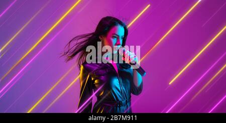 Creative emotions and neon lines on purple background, flyer, proposal. Caucasian young woman, musician singing. Concept of human emotions, facial expression, sales, ad, music, hobby. Modern art. Stock Photo