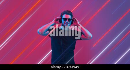 Creative emotions and neon lines on purple background, flyer, proposal. Caucasian young, musician, party DJ dancing. Concept of human emotions, facial expression, sales, ad, music, hobby. Modern art. Stock Photo