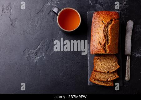 Banana, coconut bread, cake with cup of tea on slate board. Dark stone background. Copy space. Top view. Stock Photo