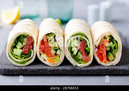 Wrap sandwich, roll with fish salmon and vegetables on cutting board. Grey background. Close up. Stock Photo