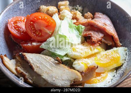 Caesar salad of grilled chicken tomatoes, lettuce, crackers and eggs. Healthy diet. On a dark background. Copy space. Stock Photo