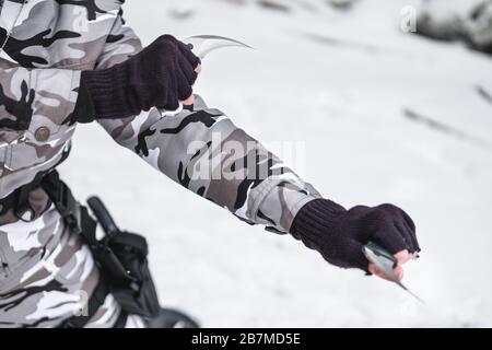 A military man in camouflage in two hands holds twisted knives. Close up. Stock Photo
