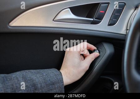 A man in a modern car. Hand pulls the lever to adjust the side mirrors of the machine. Close up. Stock Photo