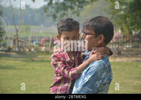 Close up of a squint eyed, strabismus, crossed eyed young boy on the lap of  a  man wearing spectacles, selective focusing Stock Photo