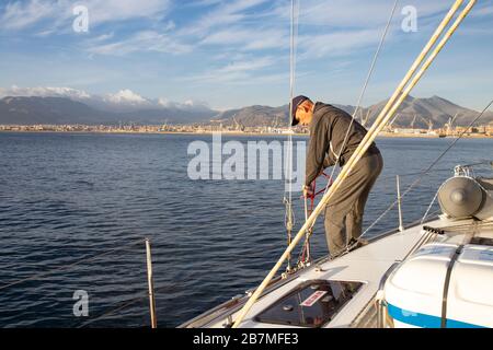 Mature sailor at steering wheel, Mast, boom and ropes. View from a sailboat to an italian harbour. Sailors world, beautiful yacht. Stock Photo