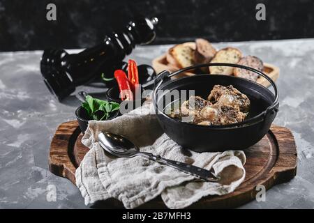 Shurpa soup in a cast-iron pot on the table on a gray background. Traditional oriental cuisine Stock Photo