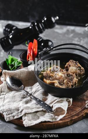 Shurpa soup in a cast-iron pot on the table on a gray background. Traditional oriental cuisine Stock Photo