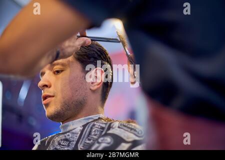 Master cuts hair and beard of men in the barbershop, hairdresser makes hairstyle for a young man Stock Photo