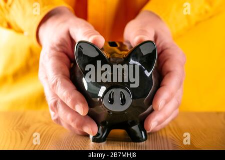 Hands protectively clasp a black piggy bank Stock Photo