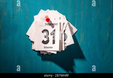 Calendar sheets are pinned to a wall. The top sheet shows the thirty-first of December with the inscription 'Silvester'. Stock Photo