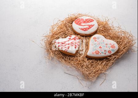 Gingerbread with heart-shaped glaze on a straw substrate on a grey textured background Stock Photo