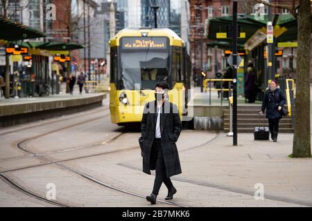 A man wearing a protective mask walks across tram lines in Manchester, the day after Prime Minister Boris Johnson called on people to stay away from pubs, clubs and theatres, work from home if possible and avoid all non-essential contacts and travel in order to reduce the impact of the coronavirus pandemic. Stock Photo