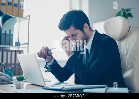 Portrait of young minded overworked student holding his glasses and touching nose-bridge while sitting at the table Stock Photo