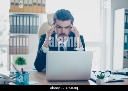 Young serious businessman in formal wear with tie touching his temples and trying to concentrate while looking at the monitor Stock Photo